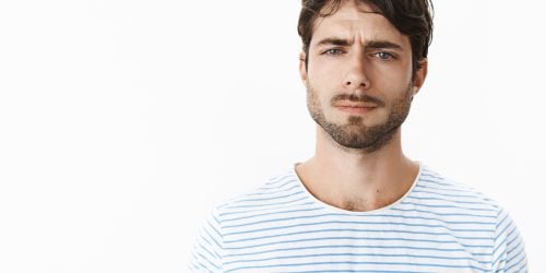 Guy looking frustrated and disappointed squinting feeling doubtful, unsure and suspicious standing confused against gray background cannot get clue why wife acting strange over gray wall. Emotions concept